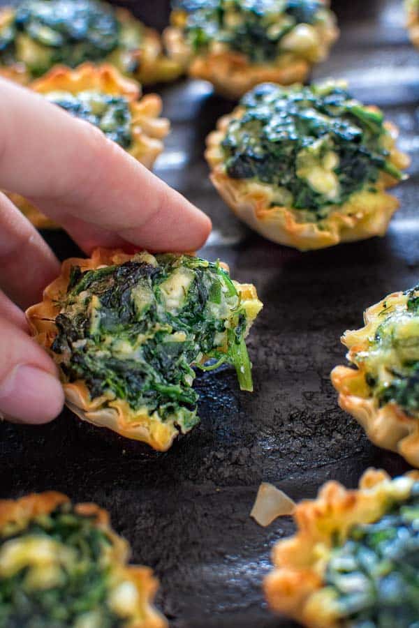 A person is holding a bite of spinach quiche.