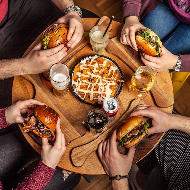 A group of people sitting around a table with hamburgers.