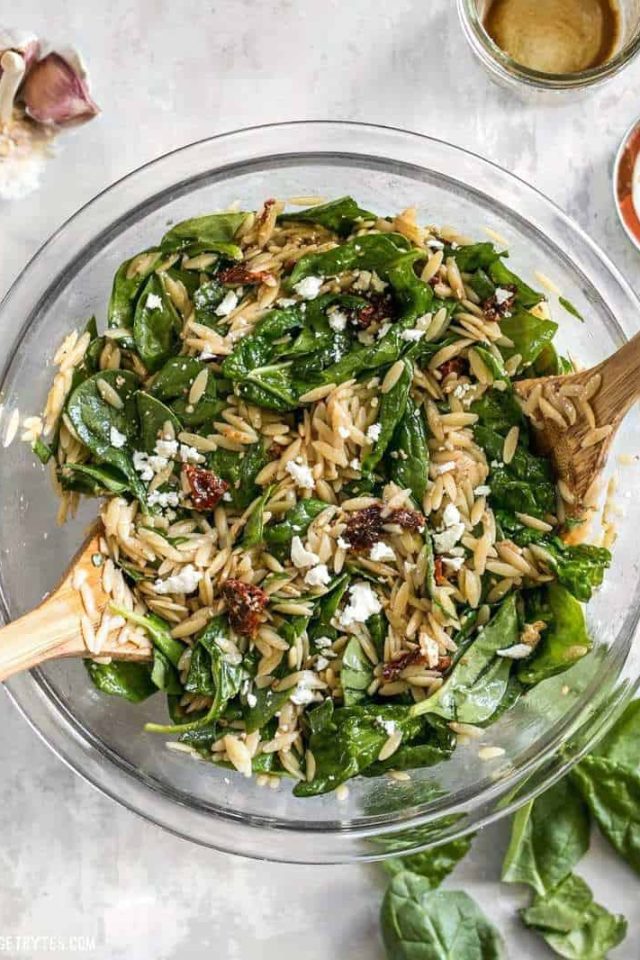 A bowl of pasta salad with spinach and pine nuts.