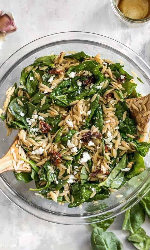 A bowl of pasta salad with spinach and pine nuts.