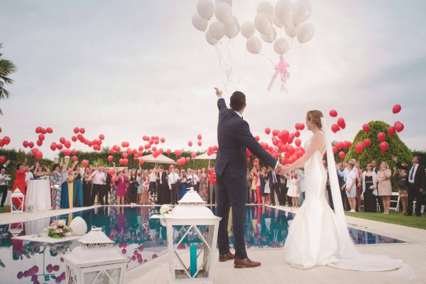 A bride and groom holding hands while standing under balloons.