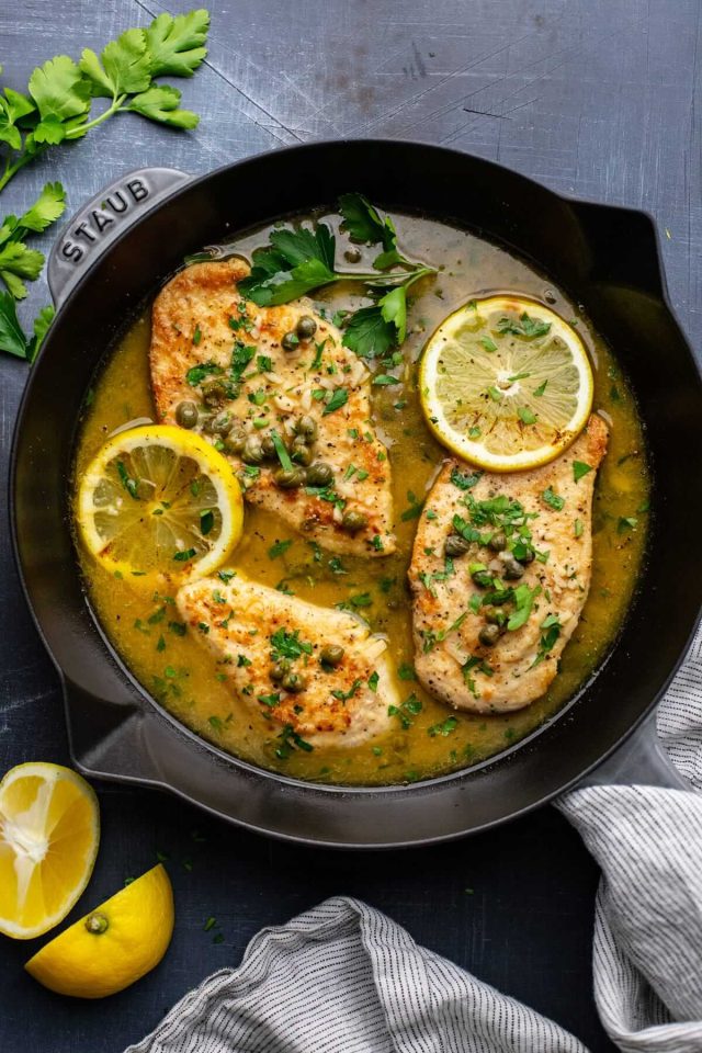 A pan of fish with lemon and parsley in it.