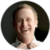 A man smiles while wearing a white shirt and tie.